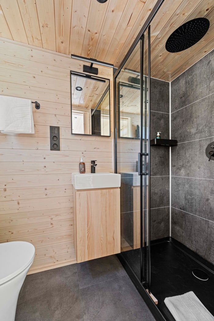 Modern bathroom with wood ceiling, glass shower, wood vanity, and dark tiled walls