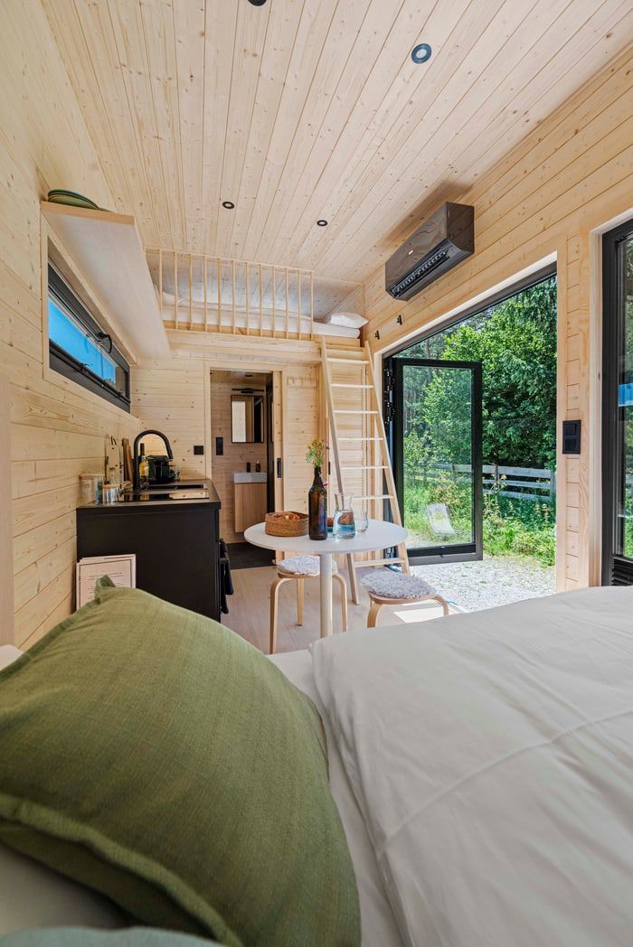 Cozy wood-paneled cabin interior with bed, desk, chair, and open sliding doors to a green patio