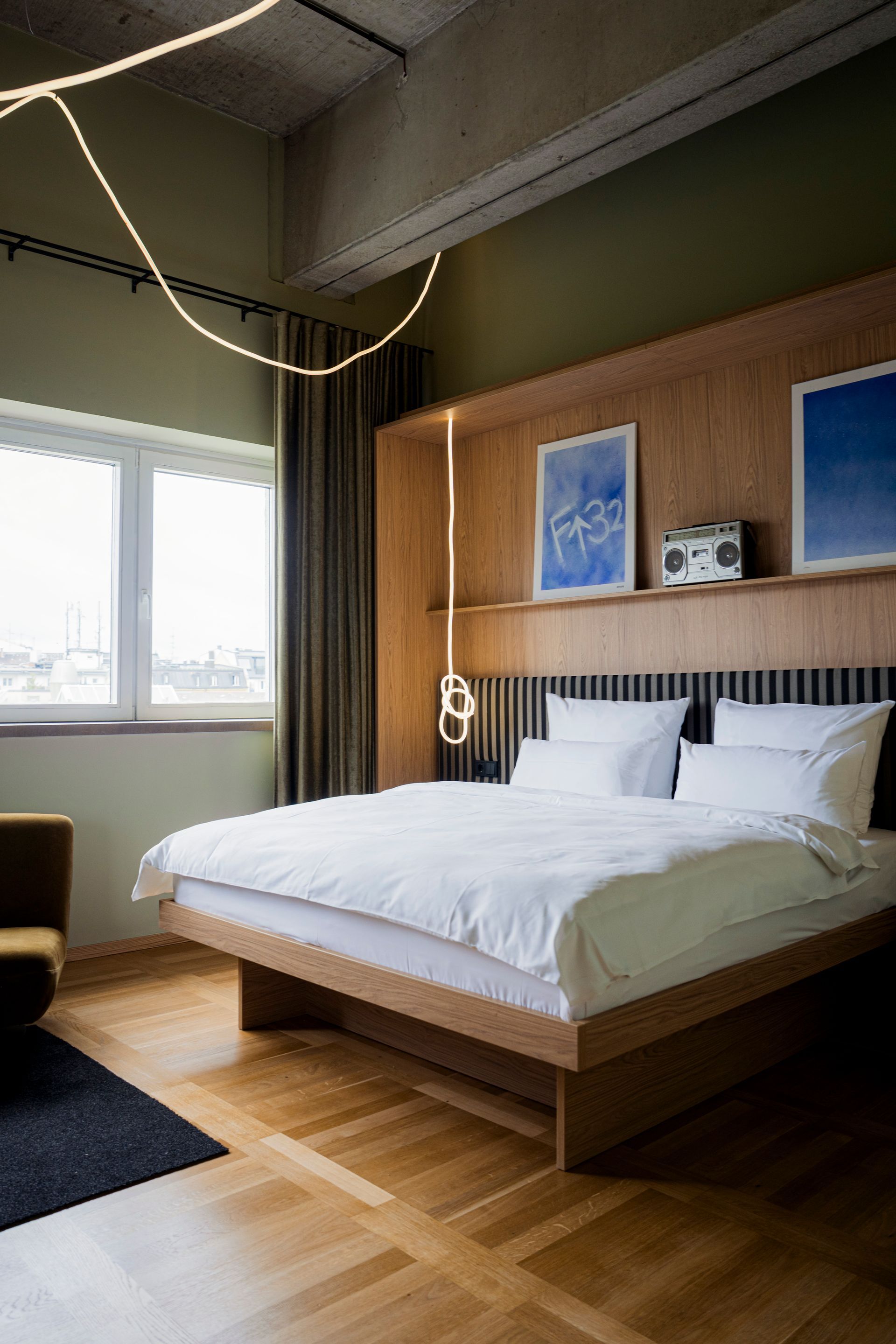Modern bedroom with white bed, wall art, brown chair, black door, window, and TV on textured wall
