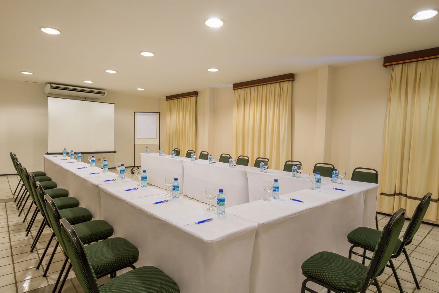 Uma sala de conferências com uma mesa longa, cadeiras e uma tela de projetor.