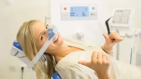 A woman is laying in a dental chair with an oxygen mask on her face.