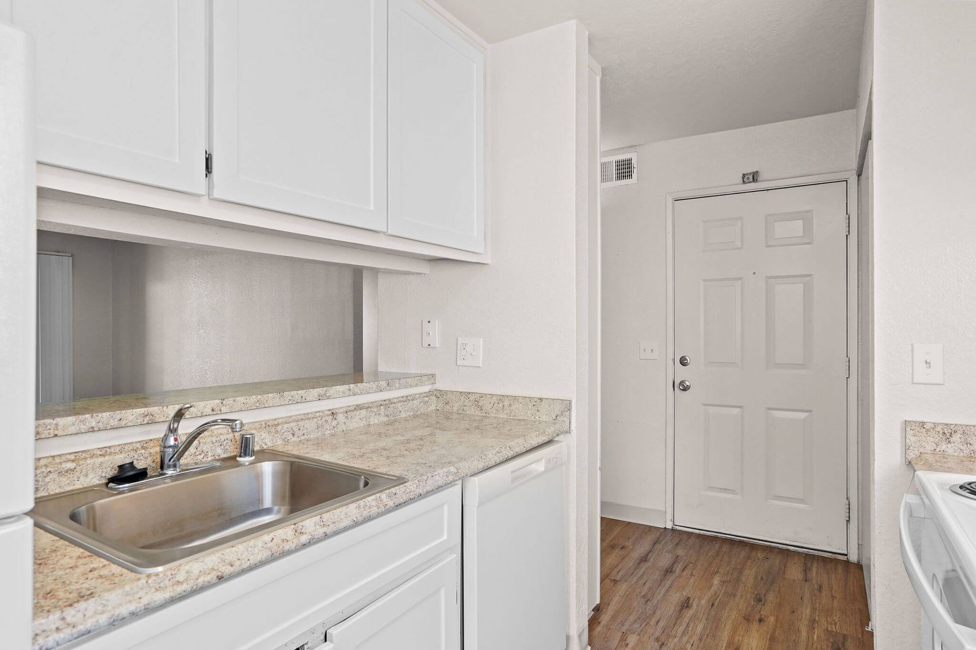 White kitchen with sink, granite countertop, cabinets, and a front door in the background