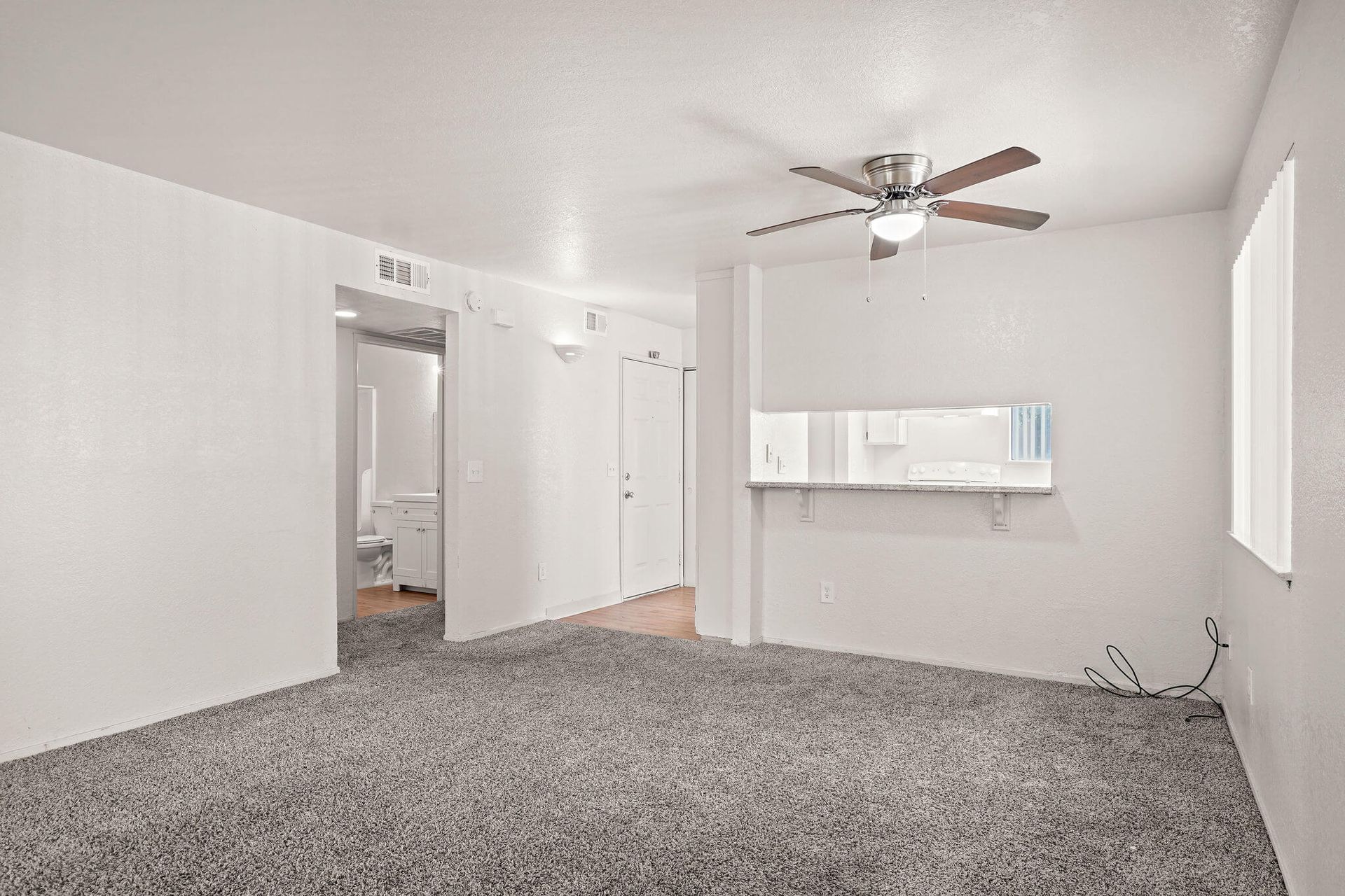 Empty white bedroom with gray carpet, ceiling fan, and small window air conditioner.