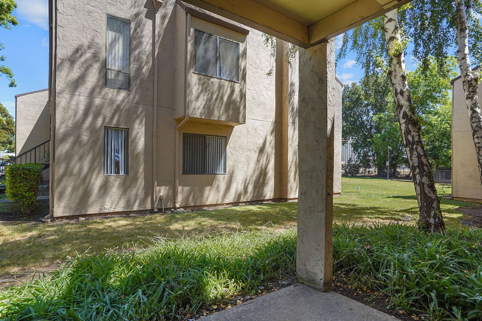 Apartment building exterior with beige walls, windows, and a covered walkway beside a grassy courtyard