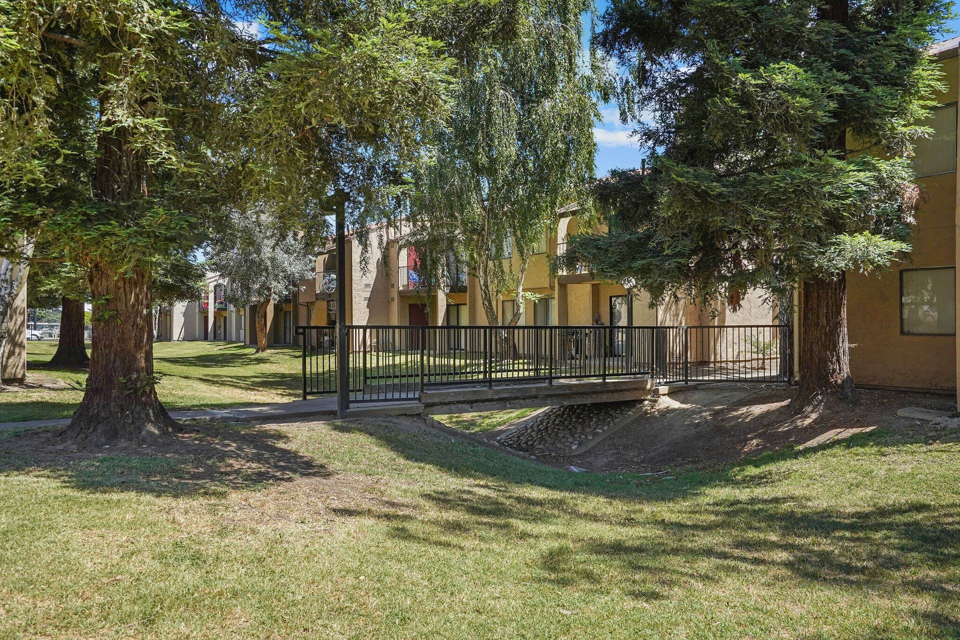 Shaded courtyard with trees, grass, and a fenced apartment building in the background