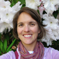A woman wearing a scarf is smiling in front of white flowers. Happy client after working with Procurement Strategy Group. 
