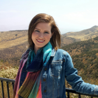 A woman in a denim jacket and scarf is standing next to a railing.