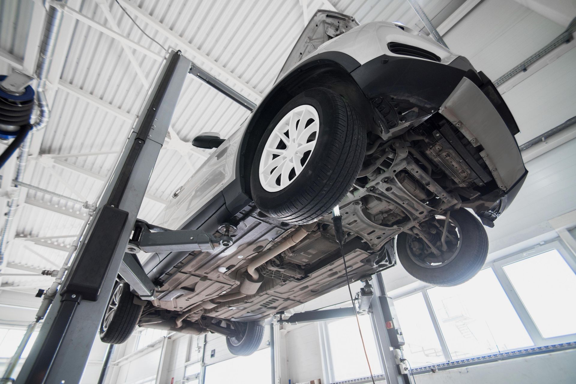 Car lifted on a hydraulic garage lift, underside visible in a bright auto repair shop
