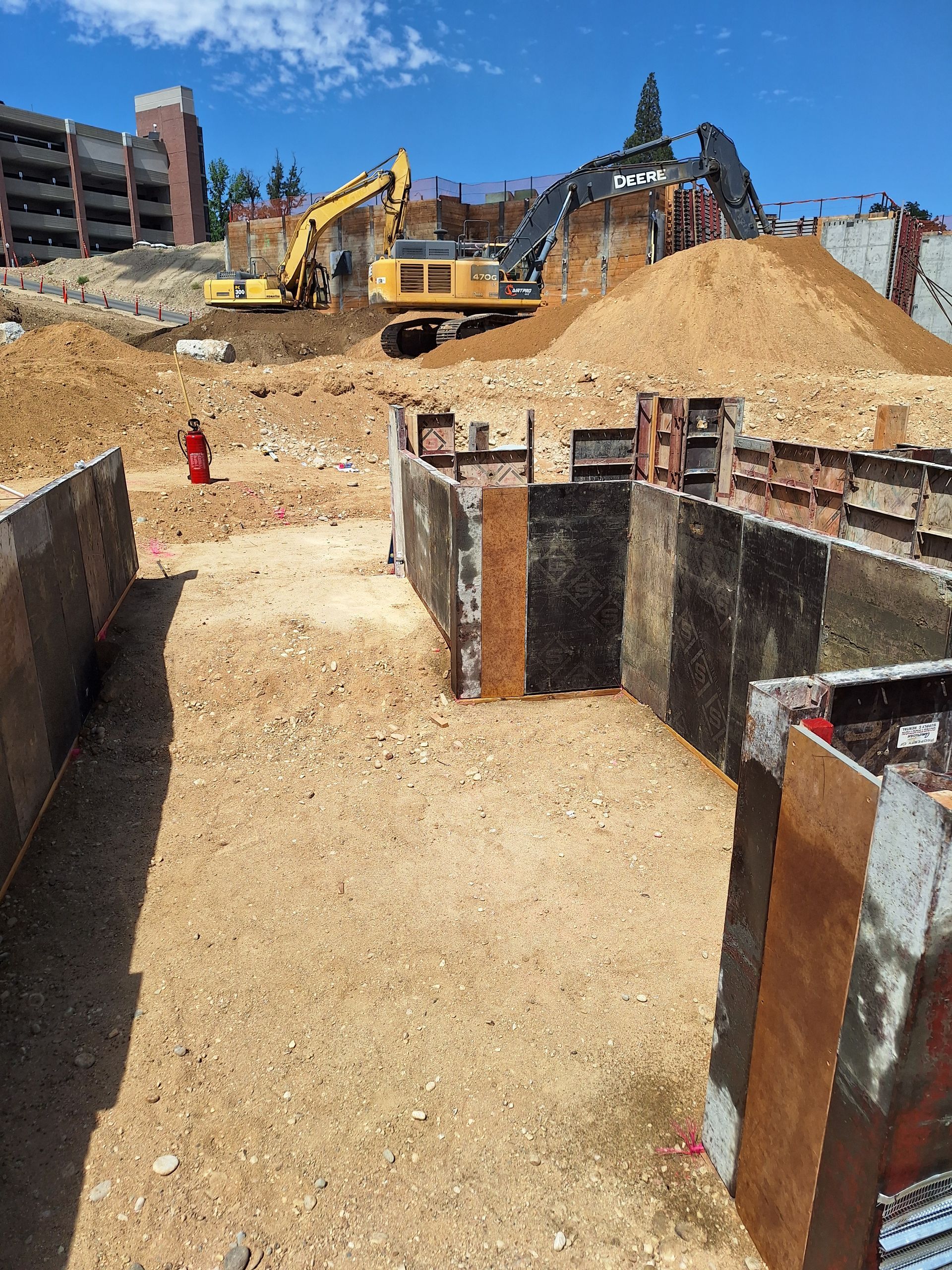 Construction site with excavation work. Heavy machinery on a dusty hillside. Ground-level view of foundation forms.