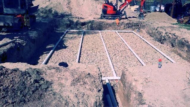 Excavated septic system with gravel, white pipes, and backhoe.