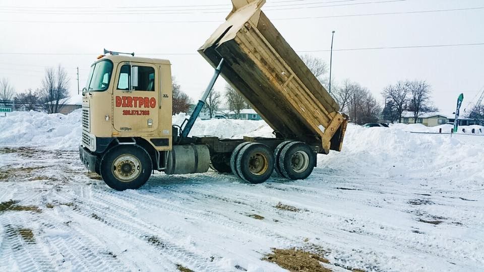 Dump truck dumping material onto a snow-covered ground, in a rural setting.