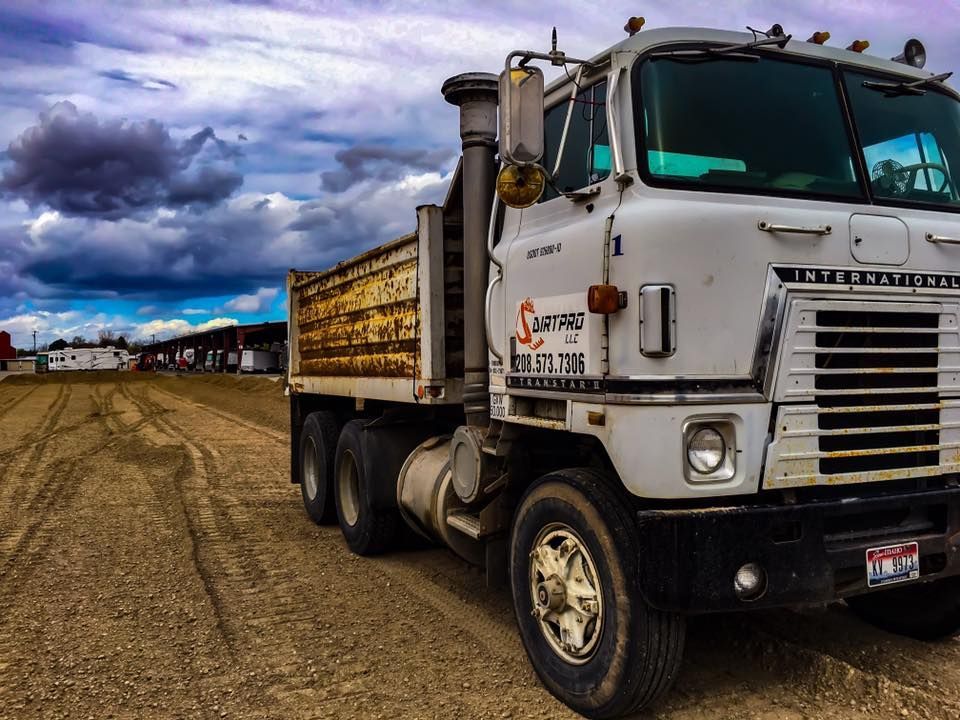 White dump truck on a dirt road under a cloudy sky.