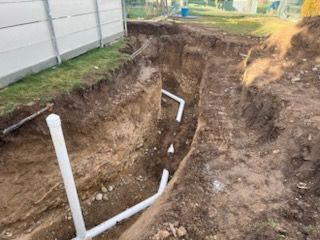 Trenches dug in yard with white PVC pipes, likely for plumbing or utilities.