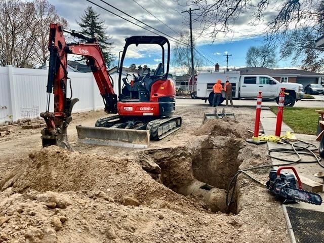 Mini excavator digging a hole in a residential area. Construction workers stand nearby.