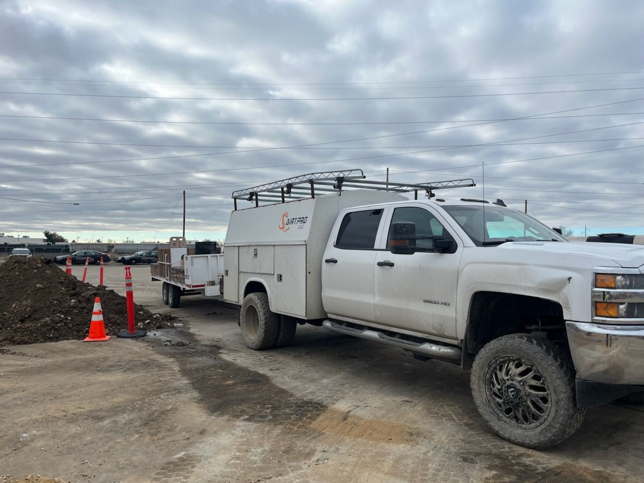 White work truck with attached trailer parked on a gravel lot under a cloudy sky.