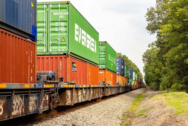 Freight train carrying stacked orange and green shipping containers on tracks beside a grassy curve