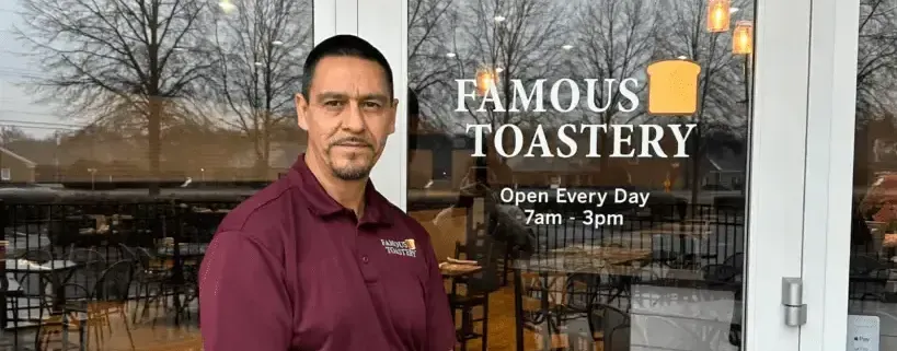 A man is standing in front of a glass door of famous toastery.