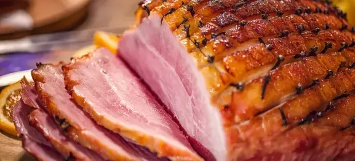 A close up of a sliced ham on a wooden cutting board.