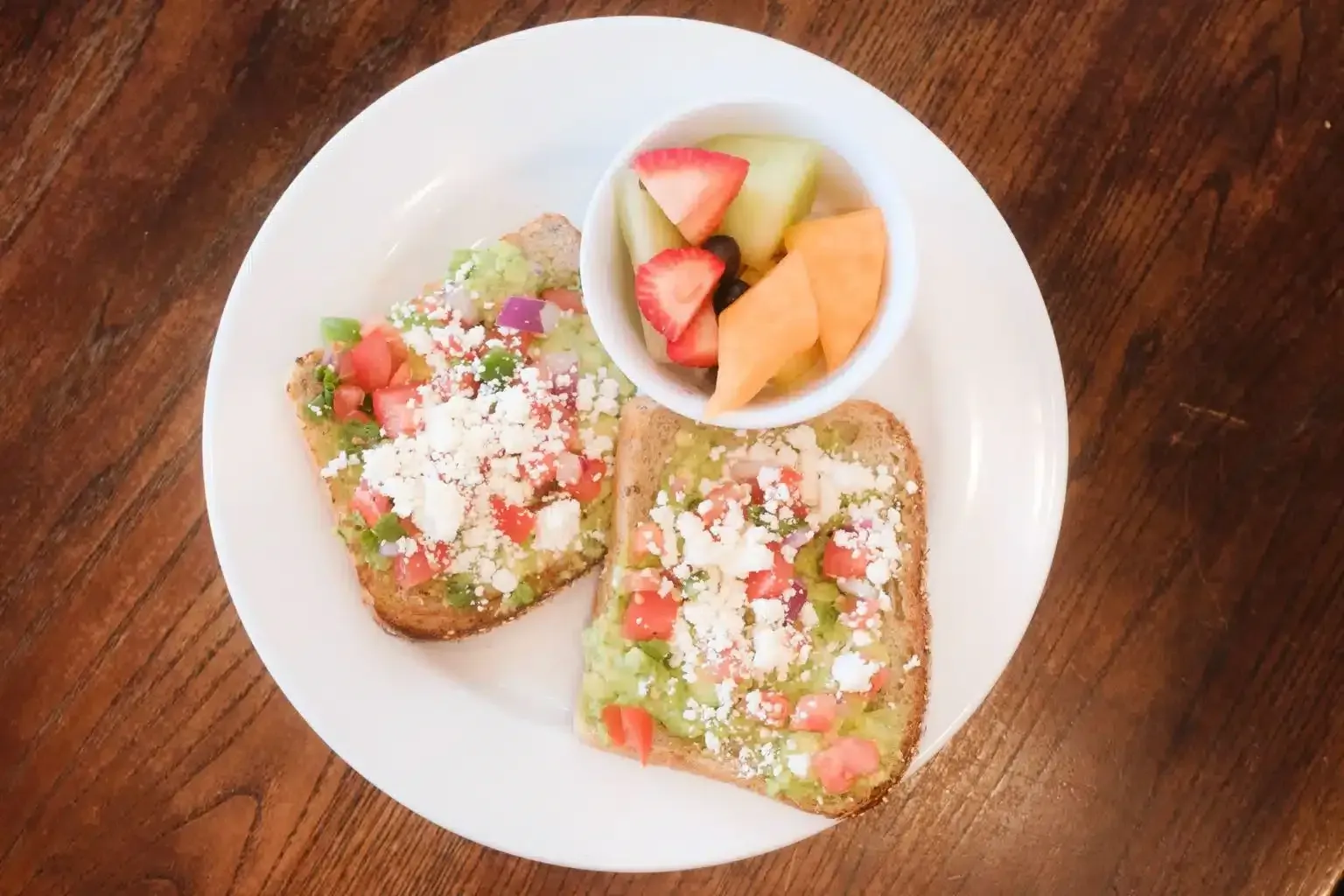 A white plate topped with two slices of toast and a bowl of fruit.