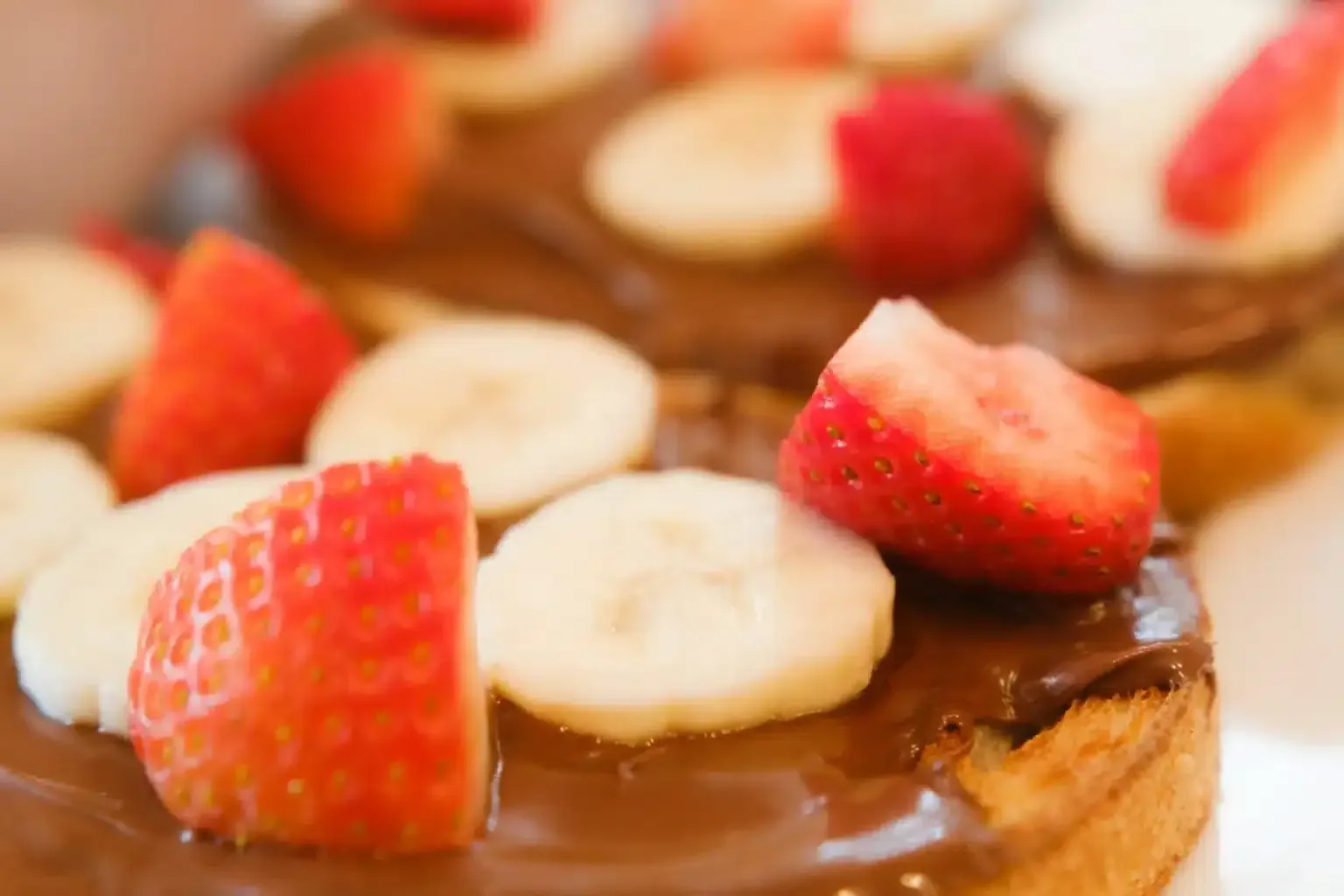 A close up of a dessert with bananas and strawberries on top.