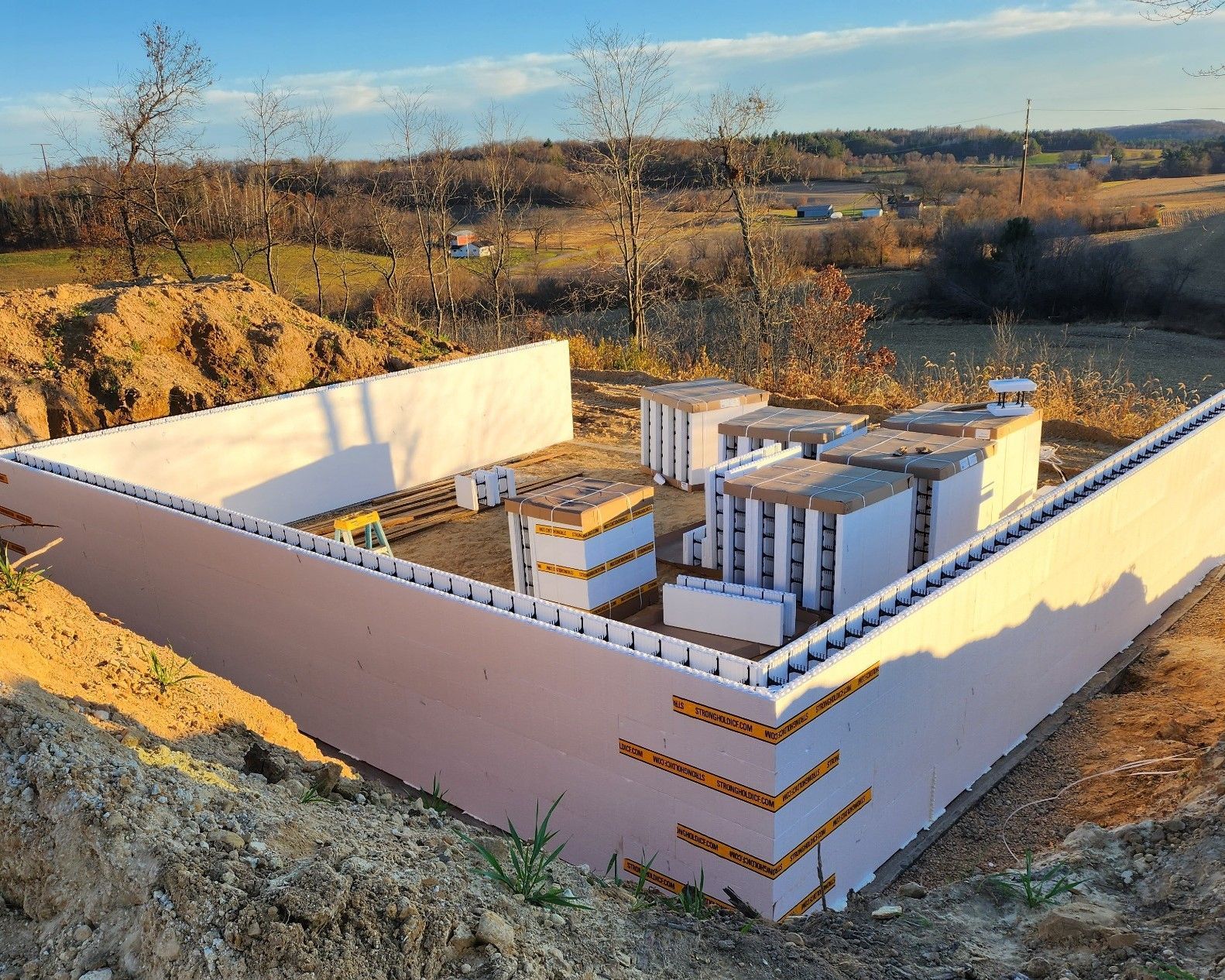 Small rural concrete foundation with white walls and dark brown exterior on a hillside field