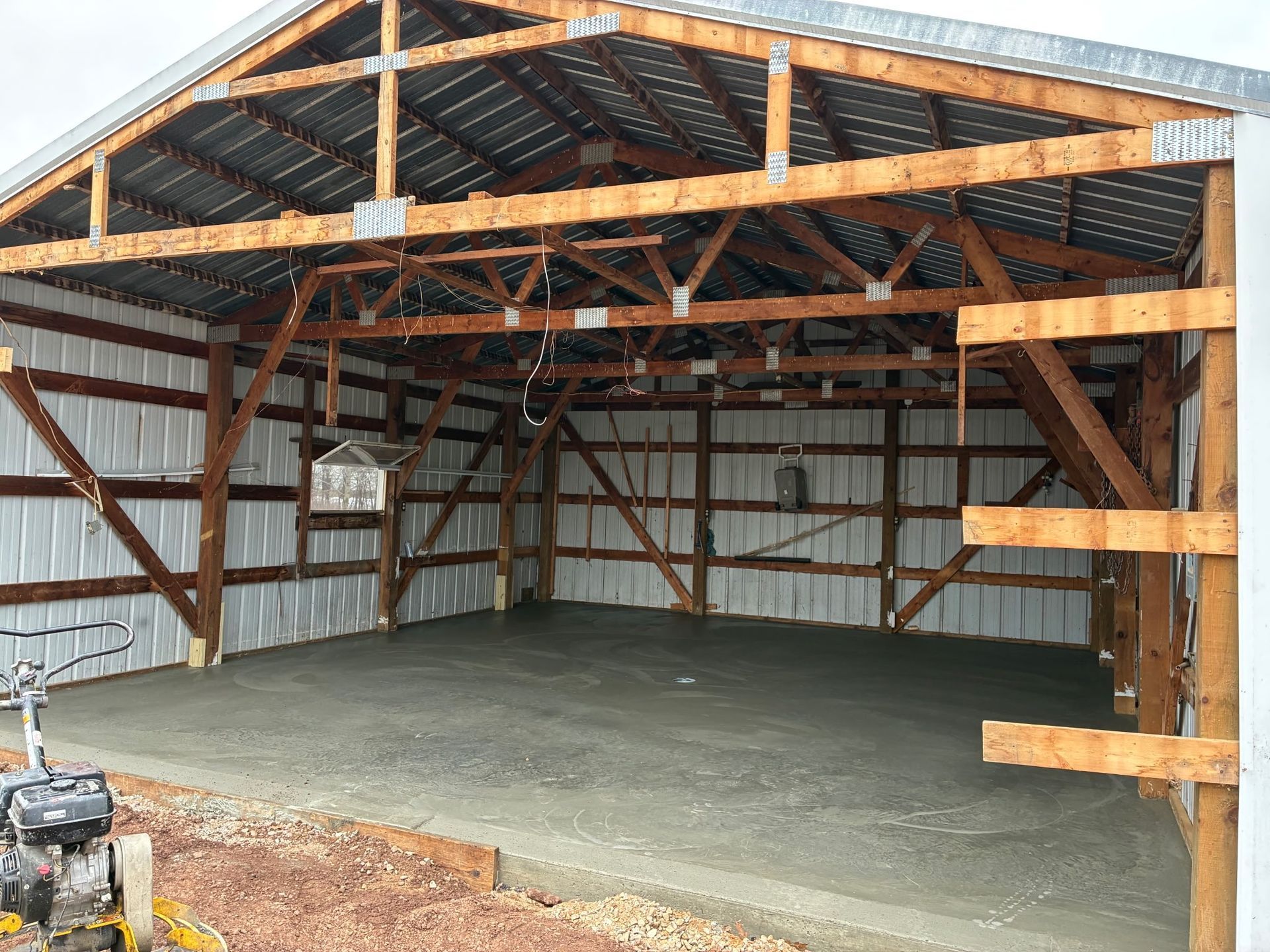 Empty wooden garage with exposed beams and a freshly poured concrete floor
