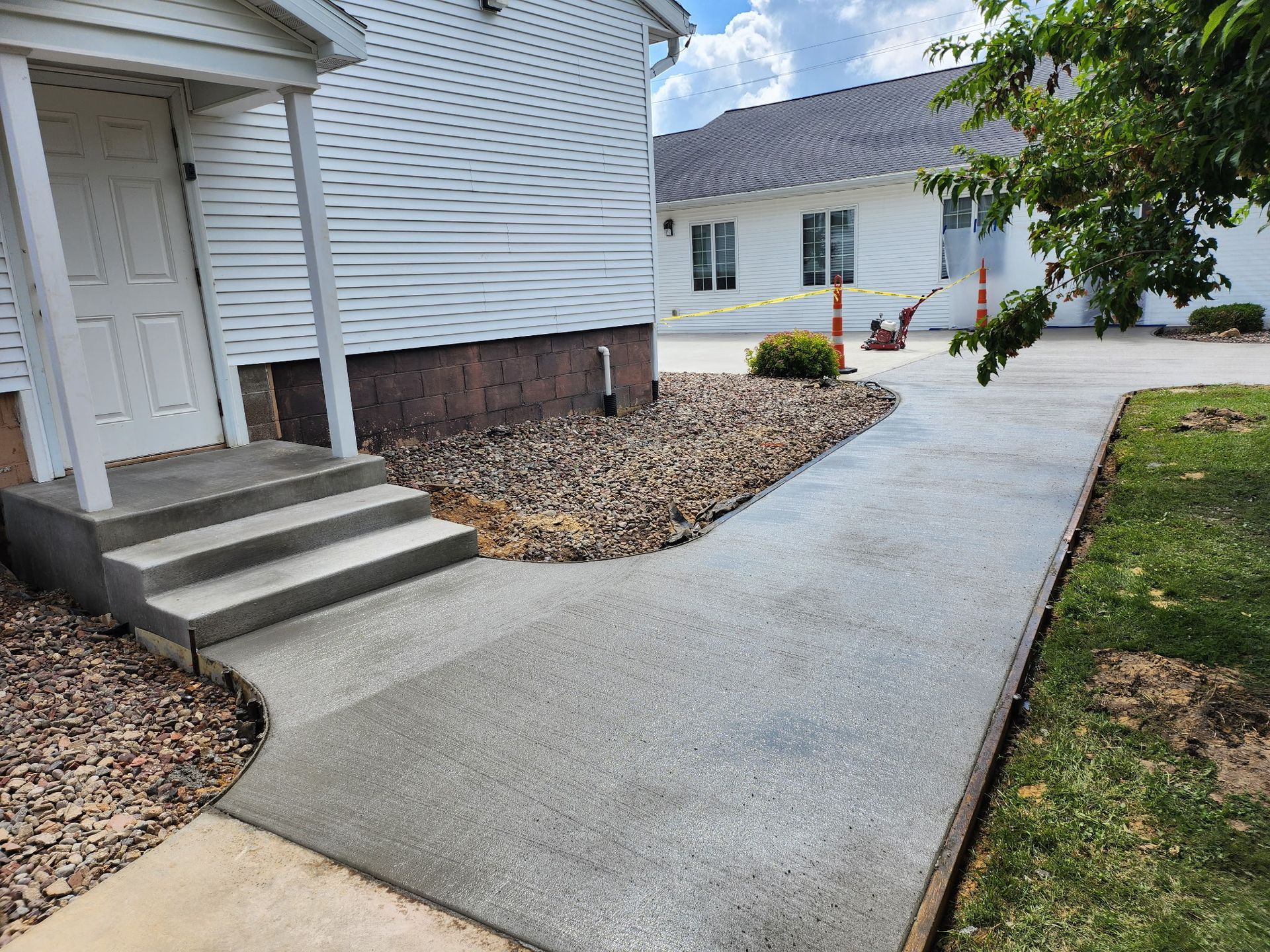 Concrete walkway beside white house with front steps and landscaped edge