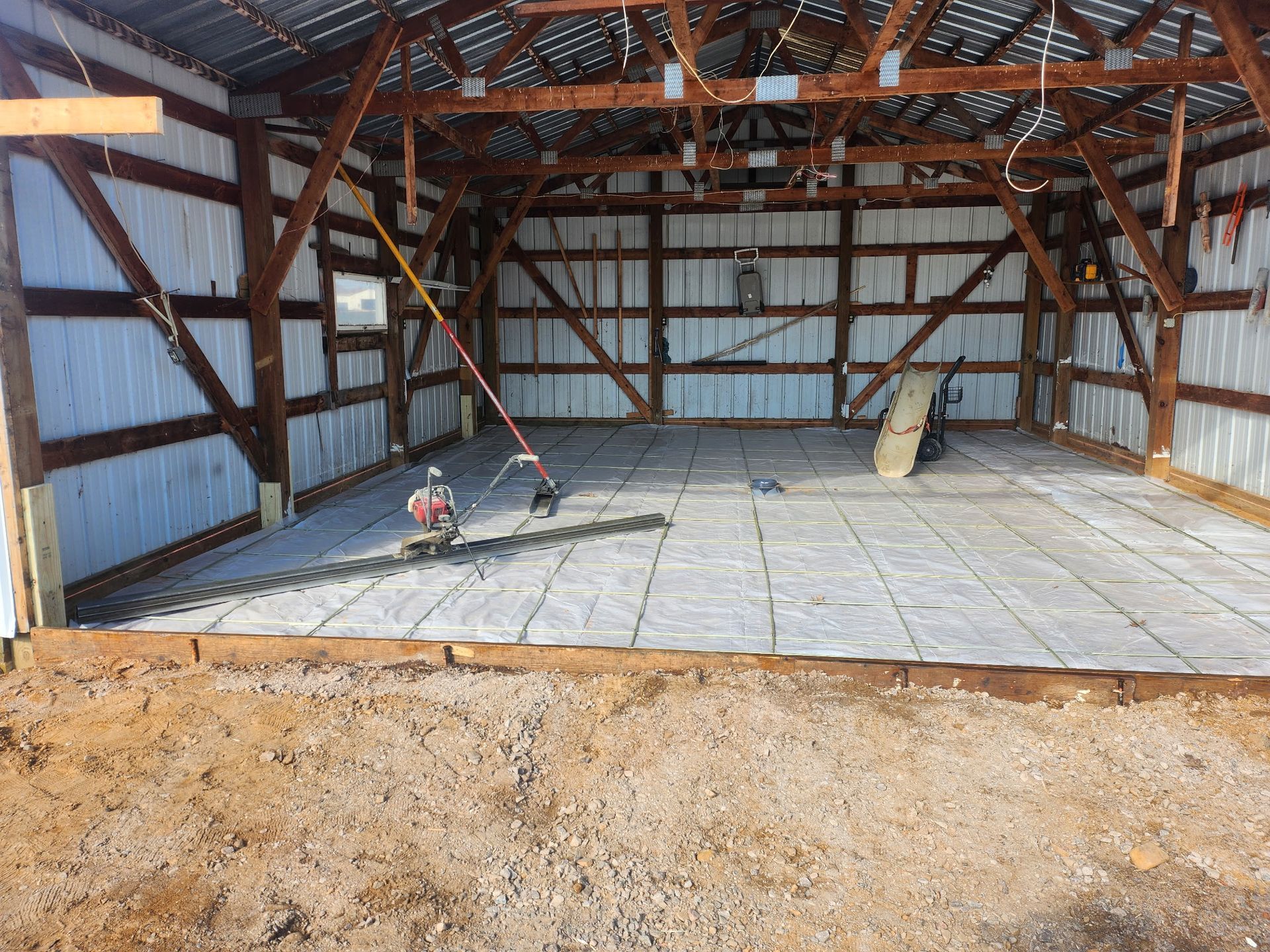 Interior of a barn under construction, with exposed wooden beams, metal walls, and a concrete floor.