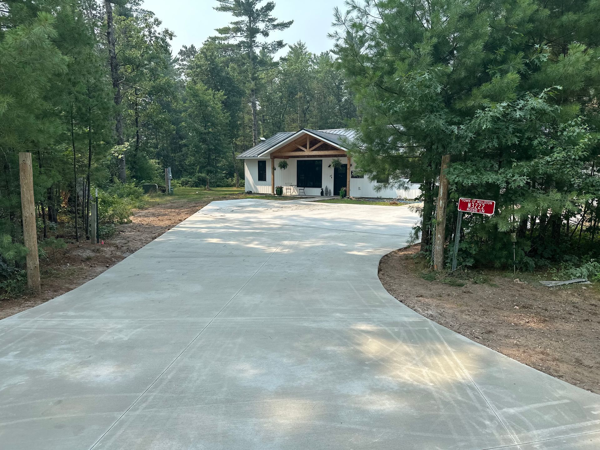 Concrete driveway leading to a small house in a wooded area, with a red mailbox on the right.