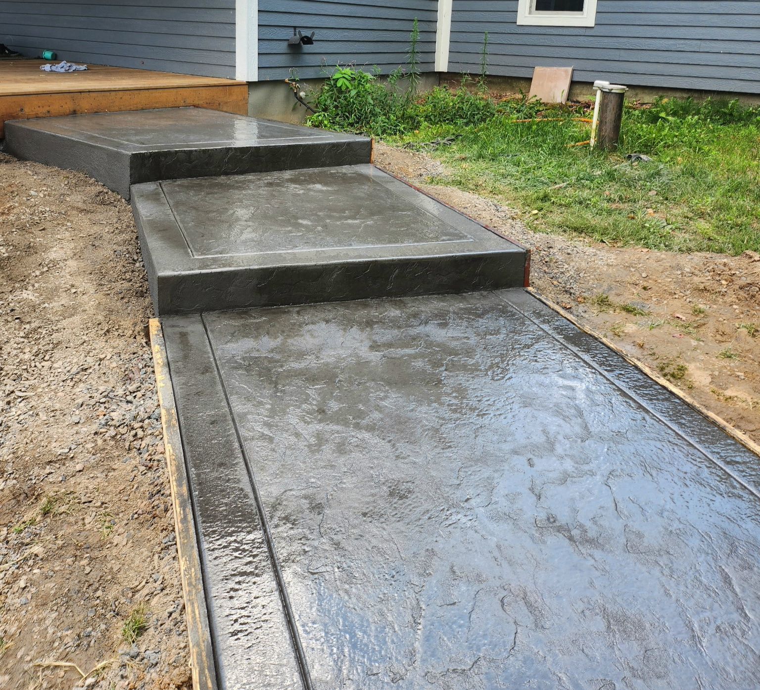 Freshly poured concrete walkway and steps beside a house and yard