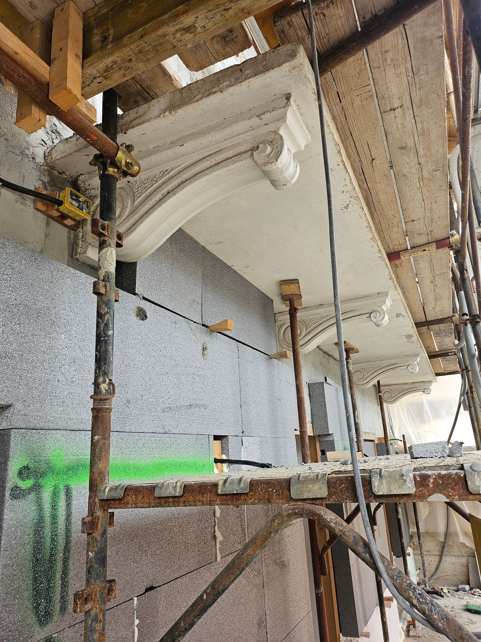 Impalcature attorno alla facciata di un edificio in costruzione, con finiture decorative bianche vicino alla linea del tetto.