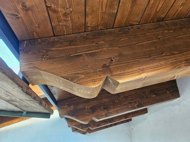 Grondaie e travi in ​​legno sotto un tetto, con la luce del sole e il cielo azzurro visibili sul bordo.