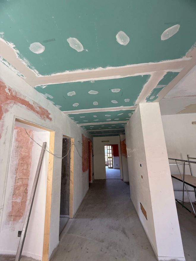 Corridoio parzialmente rifinito con soffitto color verde acqua, pareti bianche e materiali da costruzione sul pavimento.