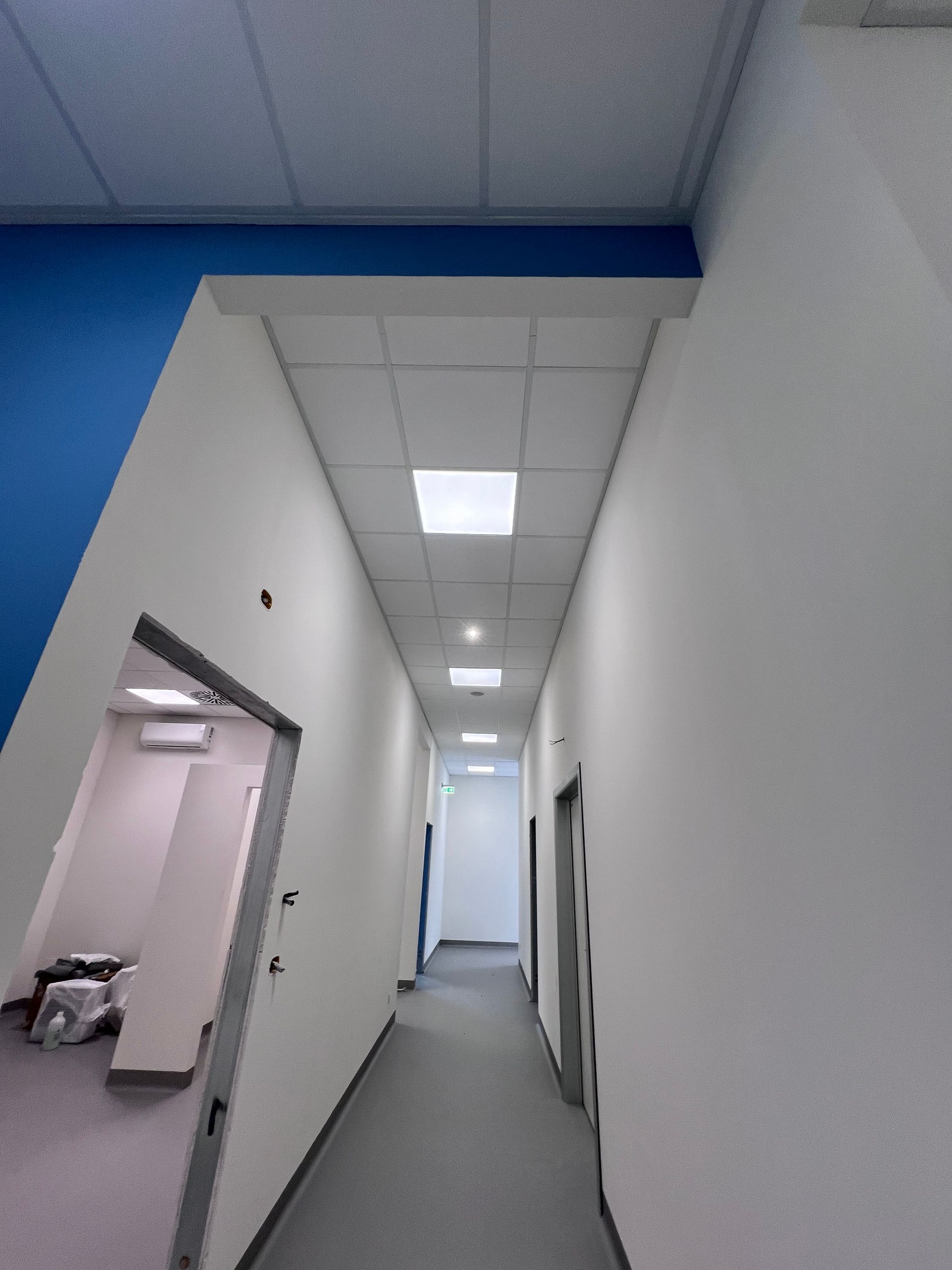 Lungo corridoio bianco con pareti blu e luci a soffitto, visto da un'estremità.