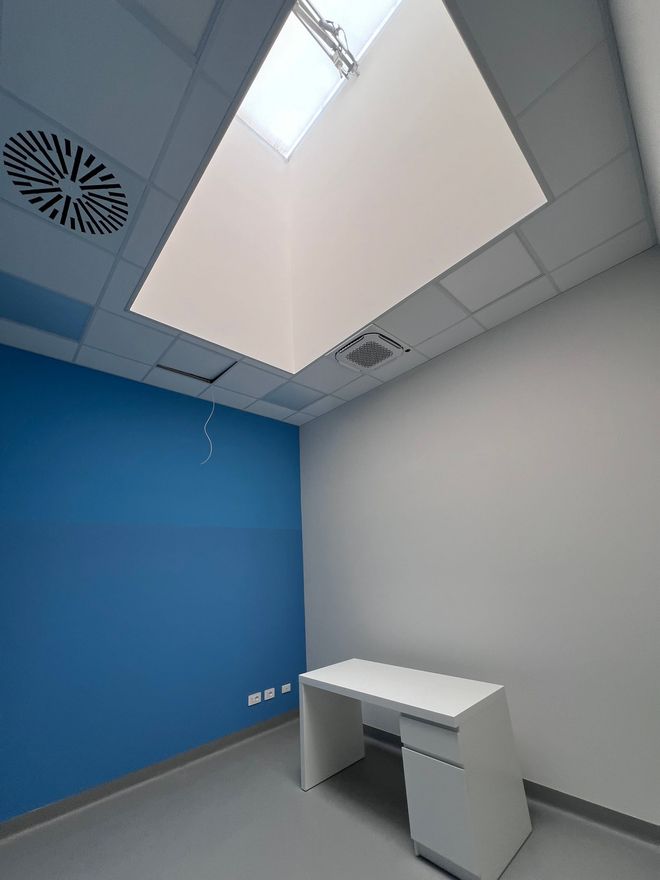 Ufficio vuoto con parete d'accento blu, scrivania bianca e lucernari sul soffitto.