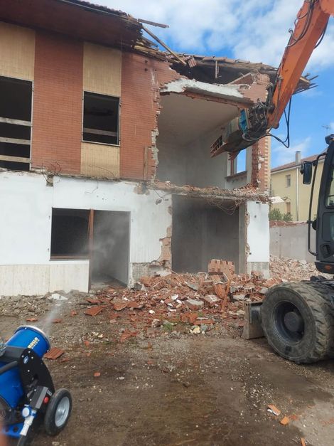 Edificio in mattoni parzialmente crollato con macerie davanti e un grosso pneumatico a terra.