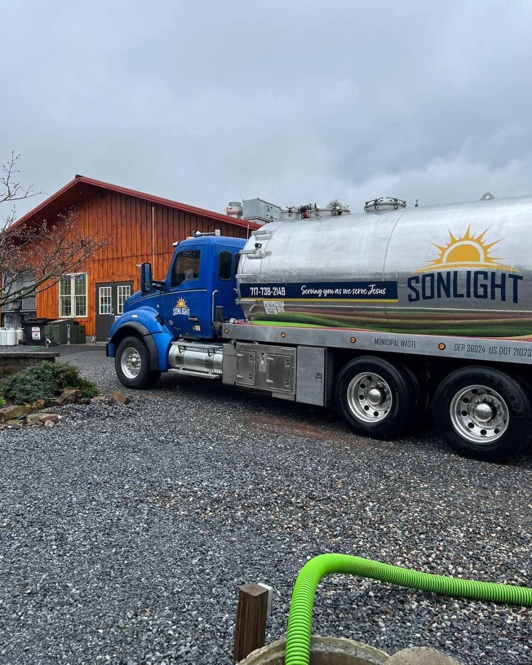 Blue tanker truck parked beside a red building on a gravel lot under cloudy skies