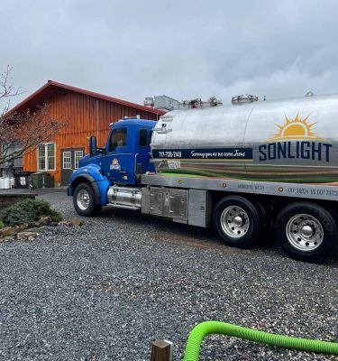 Blue tanker truck with SUNLIGHT logo parked beside a red wooden building on a gravel lot.
