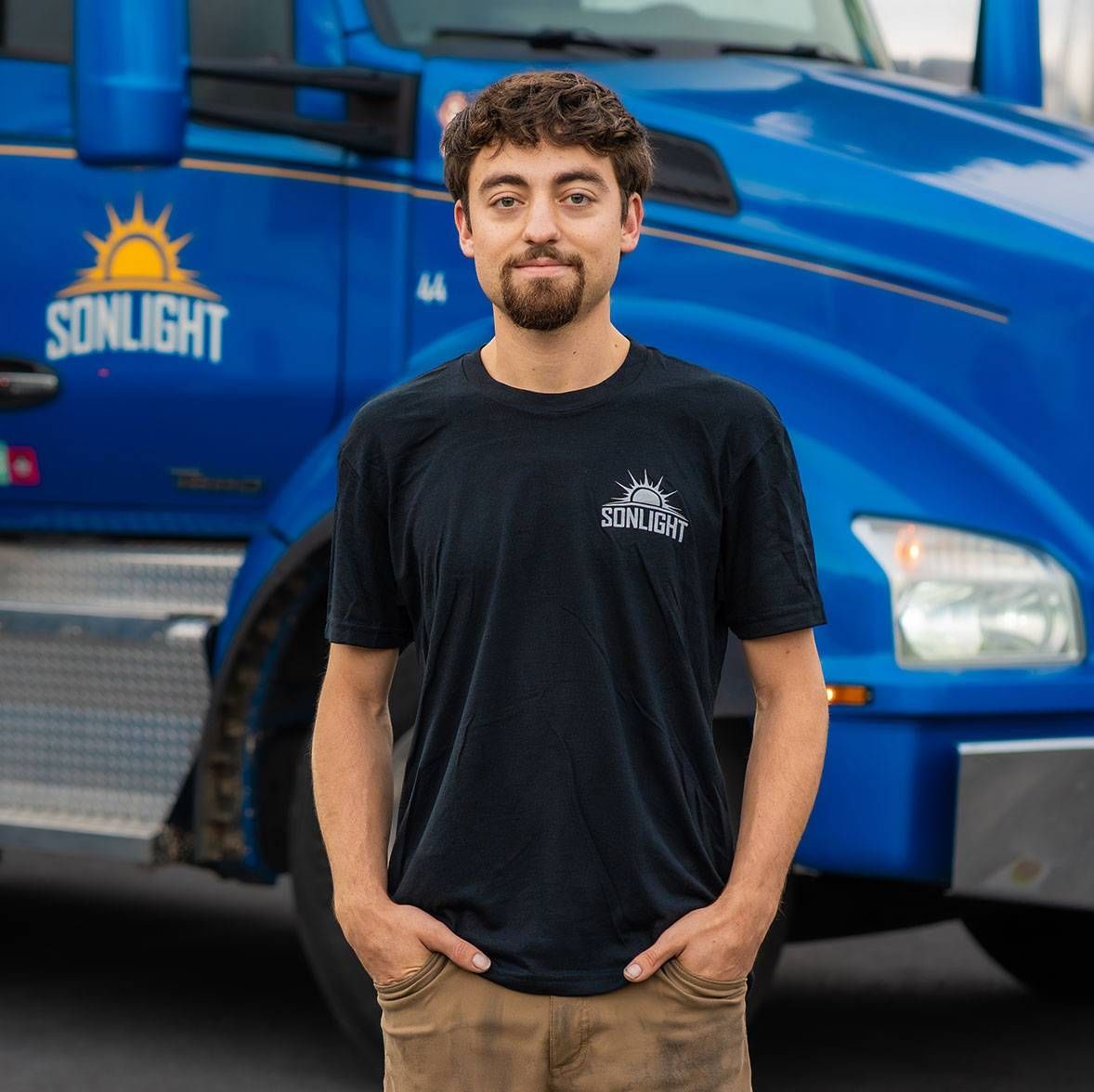 Dakota standing in front of a blue Sunlight truck, wearing a black shirt and tan pants.