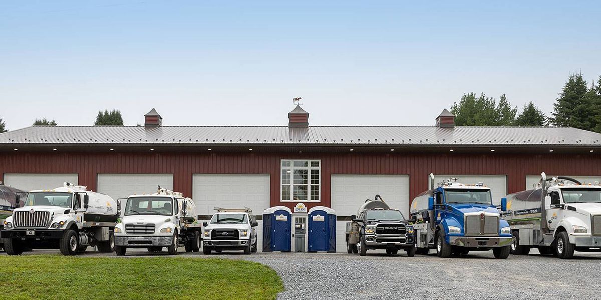 Row of work trucks and vans parked outside a low industrial building on an overcast day