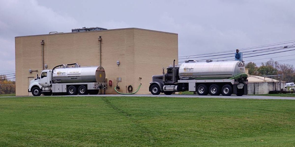 Two white tanker trucks parked beside a beige industrial building with a green grassy foreground