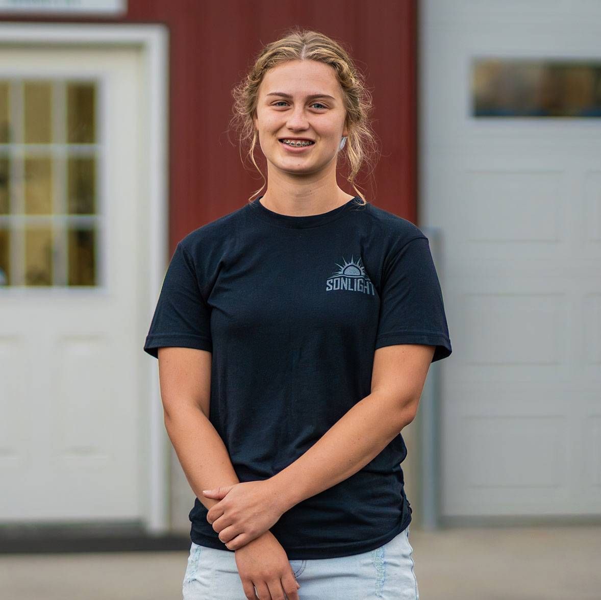 Hadassah standing outdoors in front of a building, wearing a dark T-shirt and light shorts, smiling.