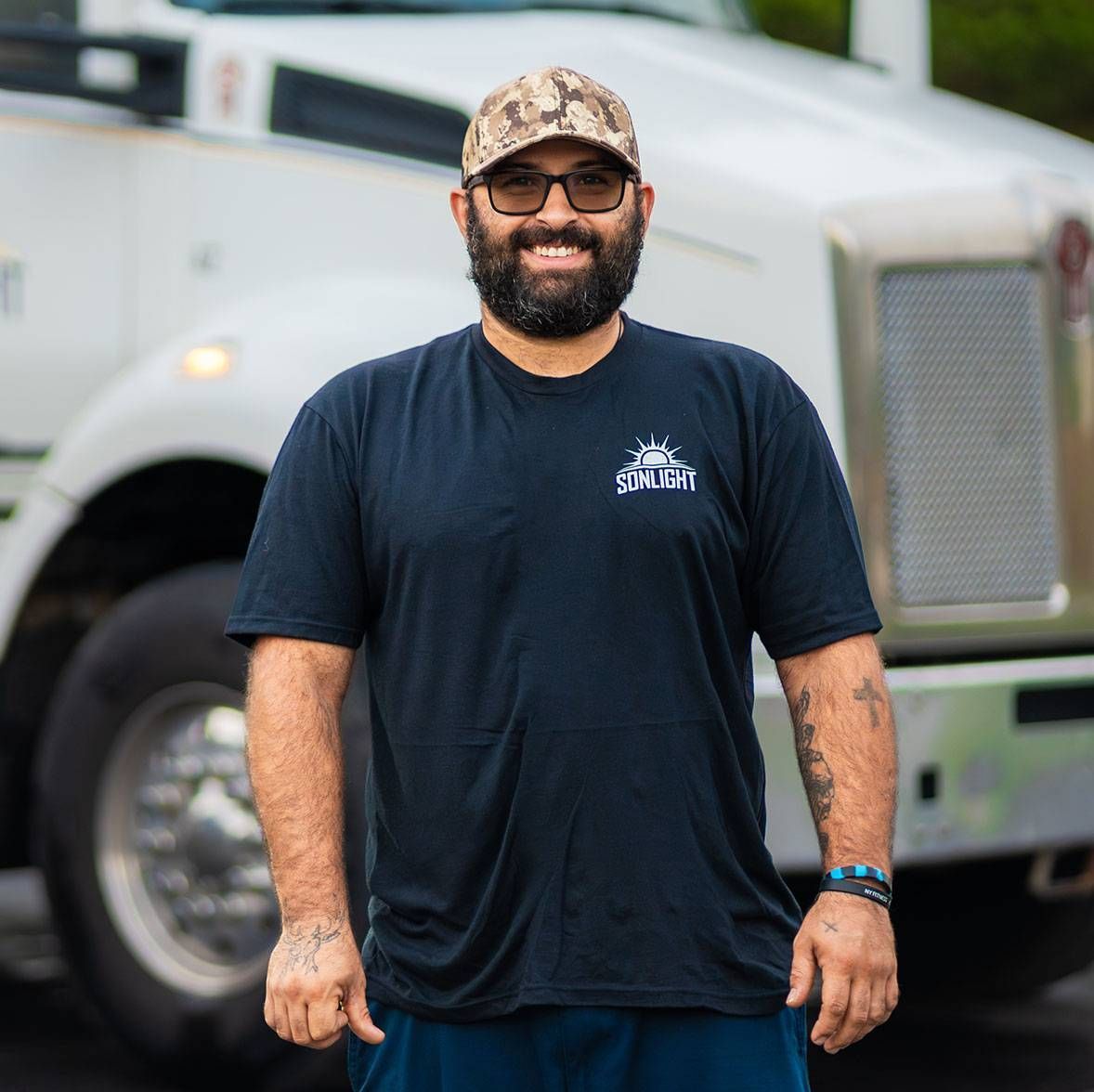 John in a navy T-shirt and camouflage cap standing in front of a white truck