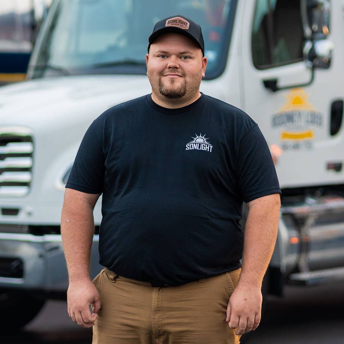 Matt standing in front of a white work truck, wearing a black cap, black T-shirt, and tan pants.