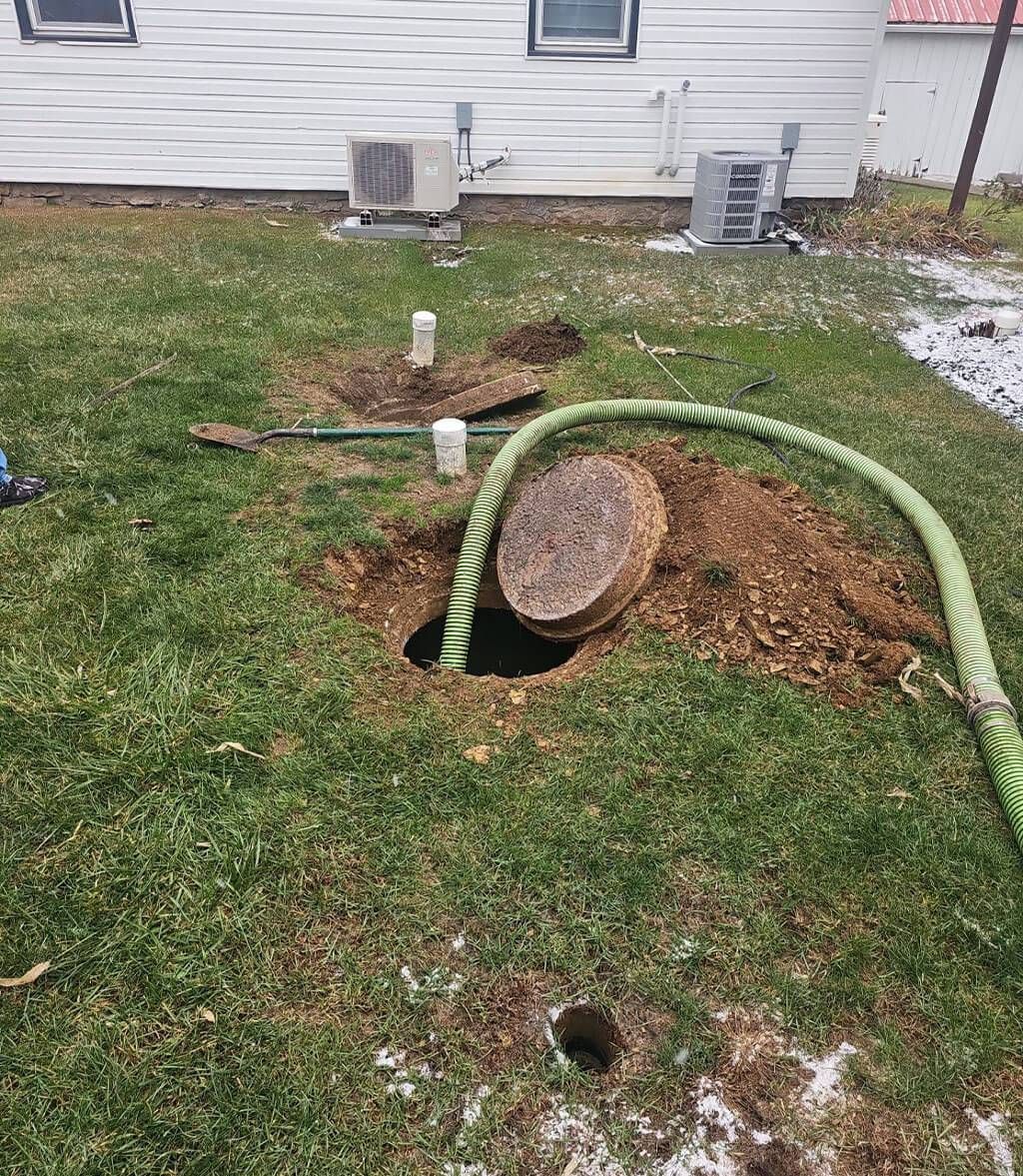 Backyard with exposed tree stump, dug-up soil, and a green hose near a house wall