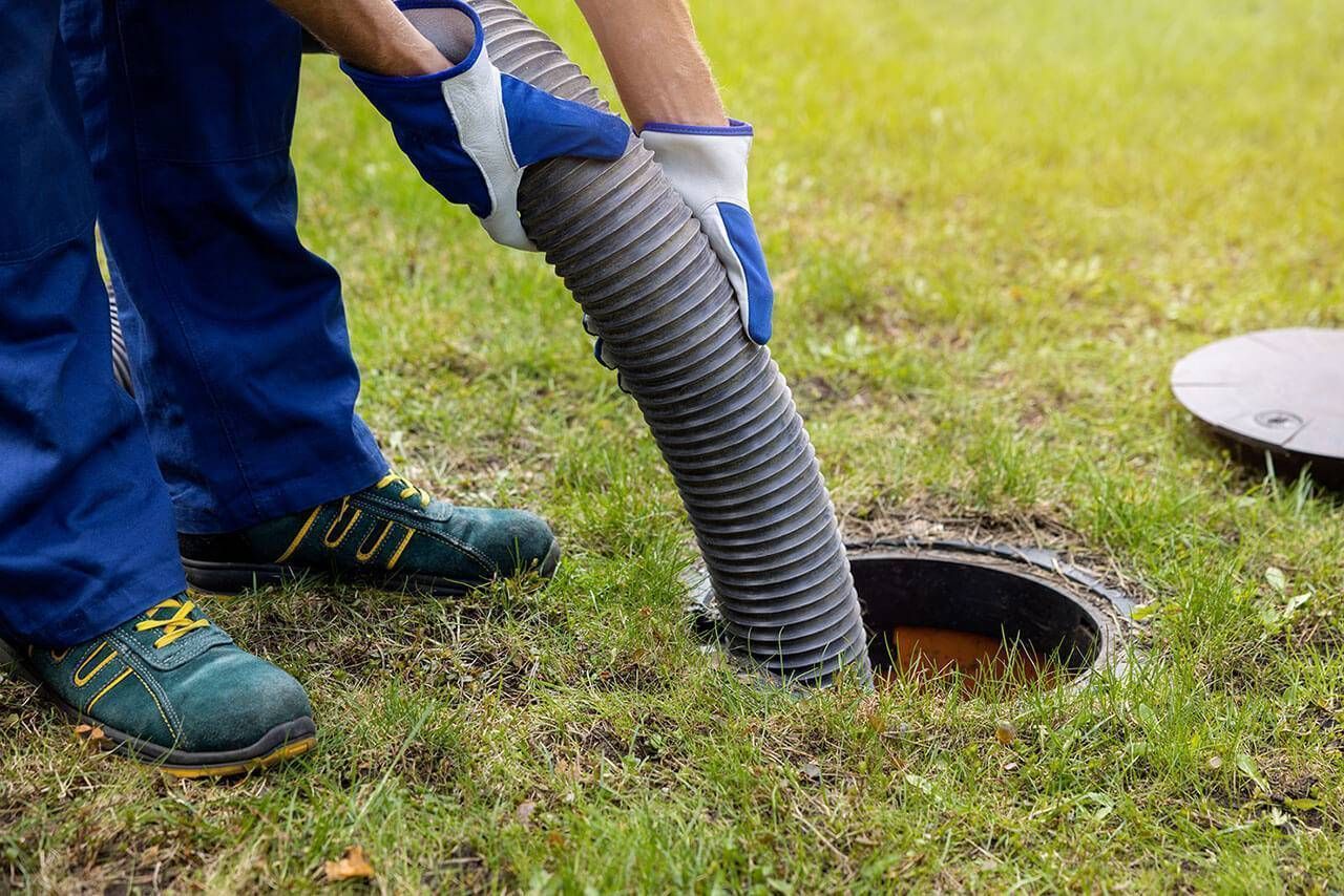 A worker in blue uniform and protective gloves uses a large flexible hose to pump out a residential septic tank.