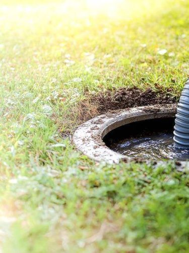 Open circular utility hole in grassy ground with a black pipe at the edge