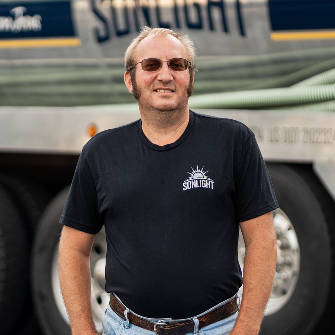 Conrad standing in front of a truck, wearing sunglasses, a black T-shirt, and jeans, with a slight smile.