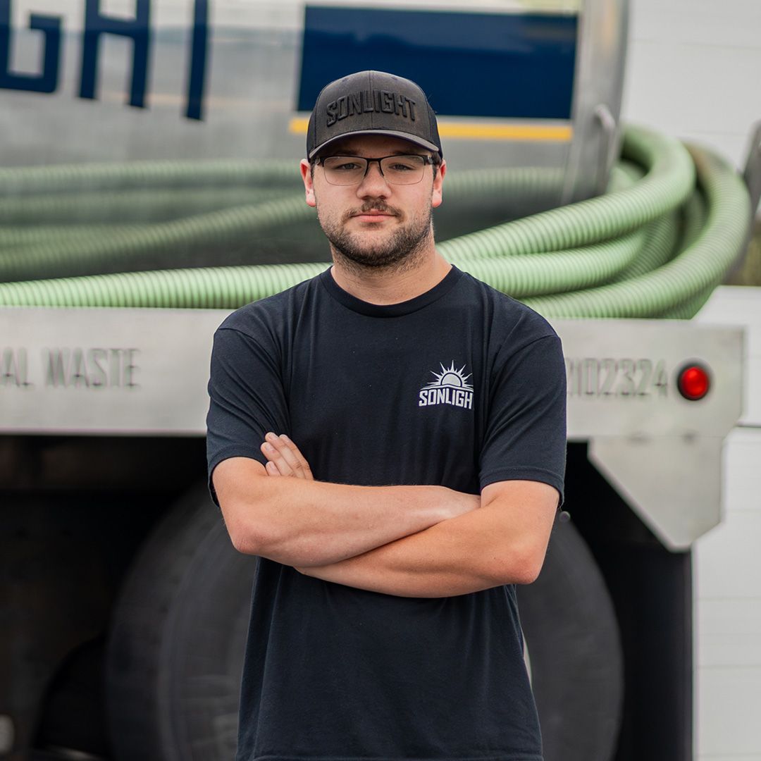 Issac standing beside a blue tanker truck in a parking lot, wearing dark jacket and cap.