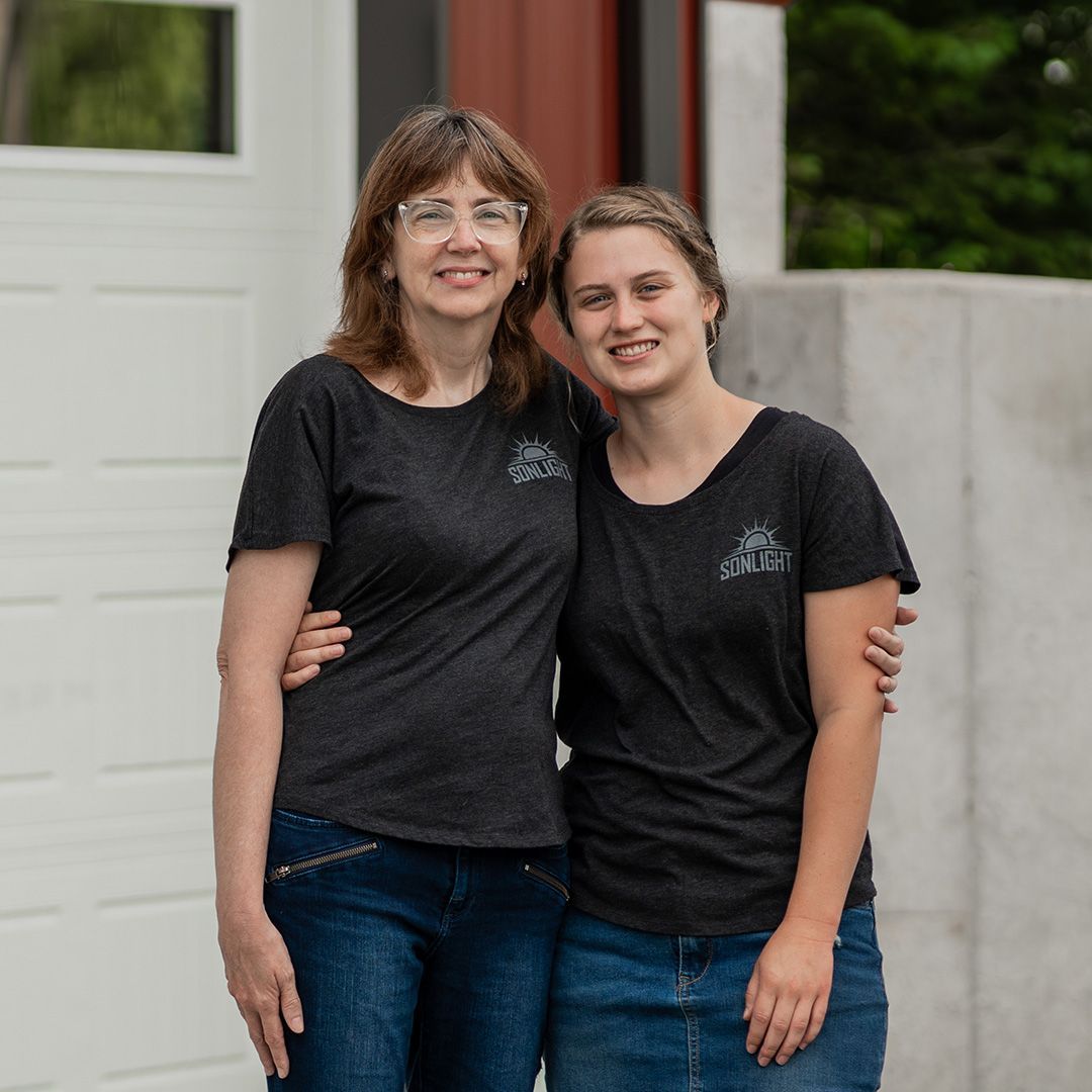 Two women in black T-shirts standing together and smiling outdoors by a building entrance